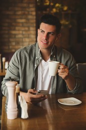 Man with smartphone listening to audiobook at table in cafe