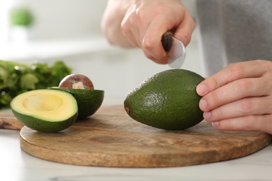 Man cutting avocado for delicious smoothie at white table, closeup