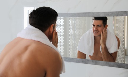 Photo of Handsome man touching his smooth face after shaving near mirror in bathroom