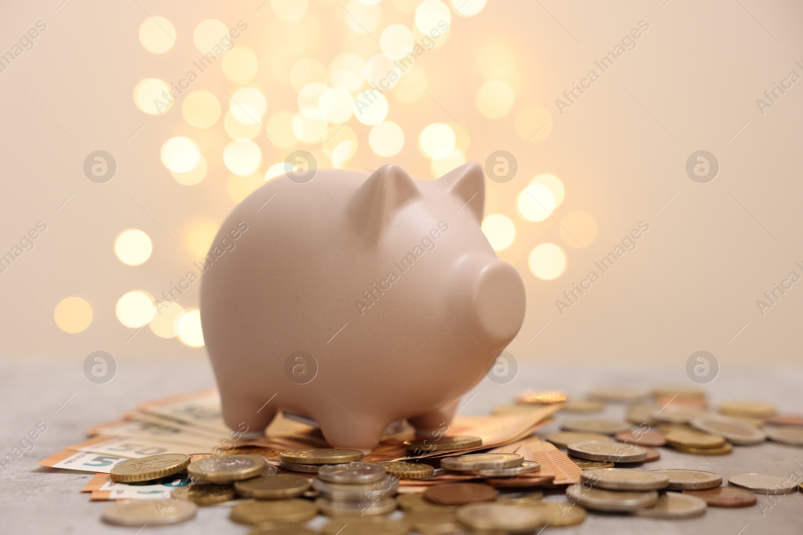 Piggy bank and coins on grey table against blurred lights Photo of Piggy bank and coins on grey table against blurred lights