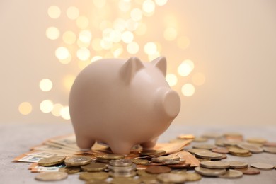 Photo of Piggy bank and coins on grey table against blurred lights