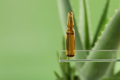 Photo of Skincare ampoule near aloe vera on light green background, closeup. Space for text