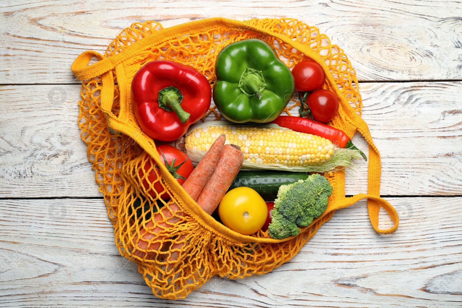 Photo of Net bag with different fresh vegetables on white wooden table, top view