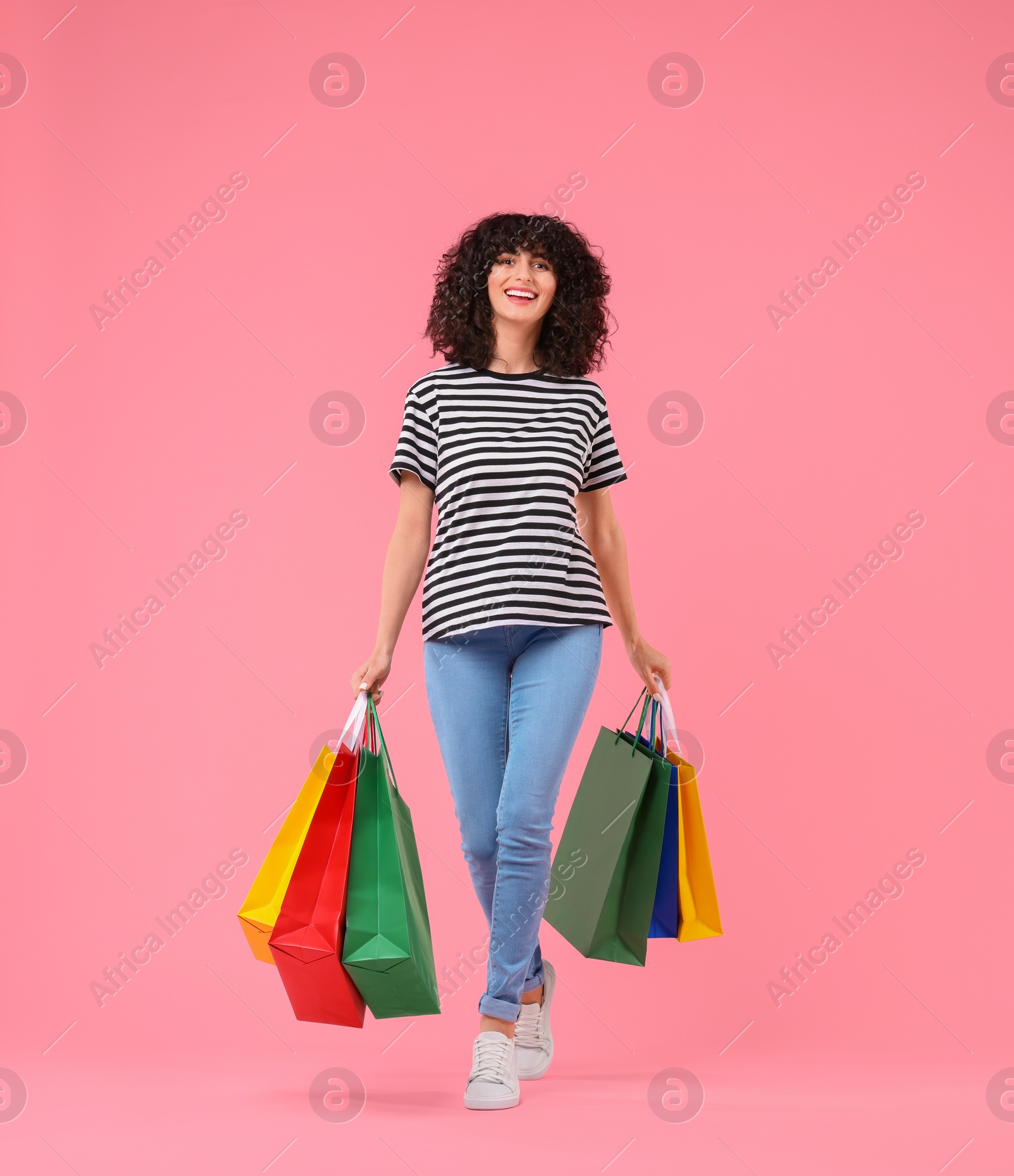 Photo of Happy young woman with shopping bags on pink background