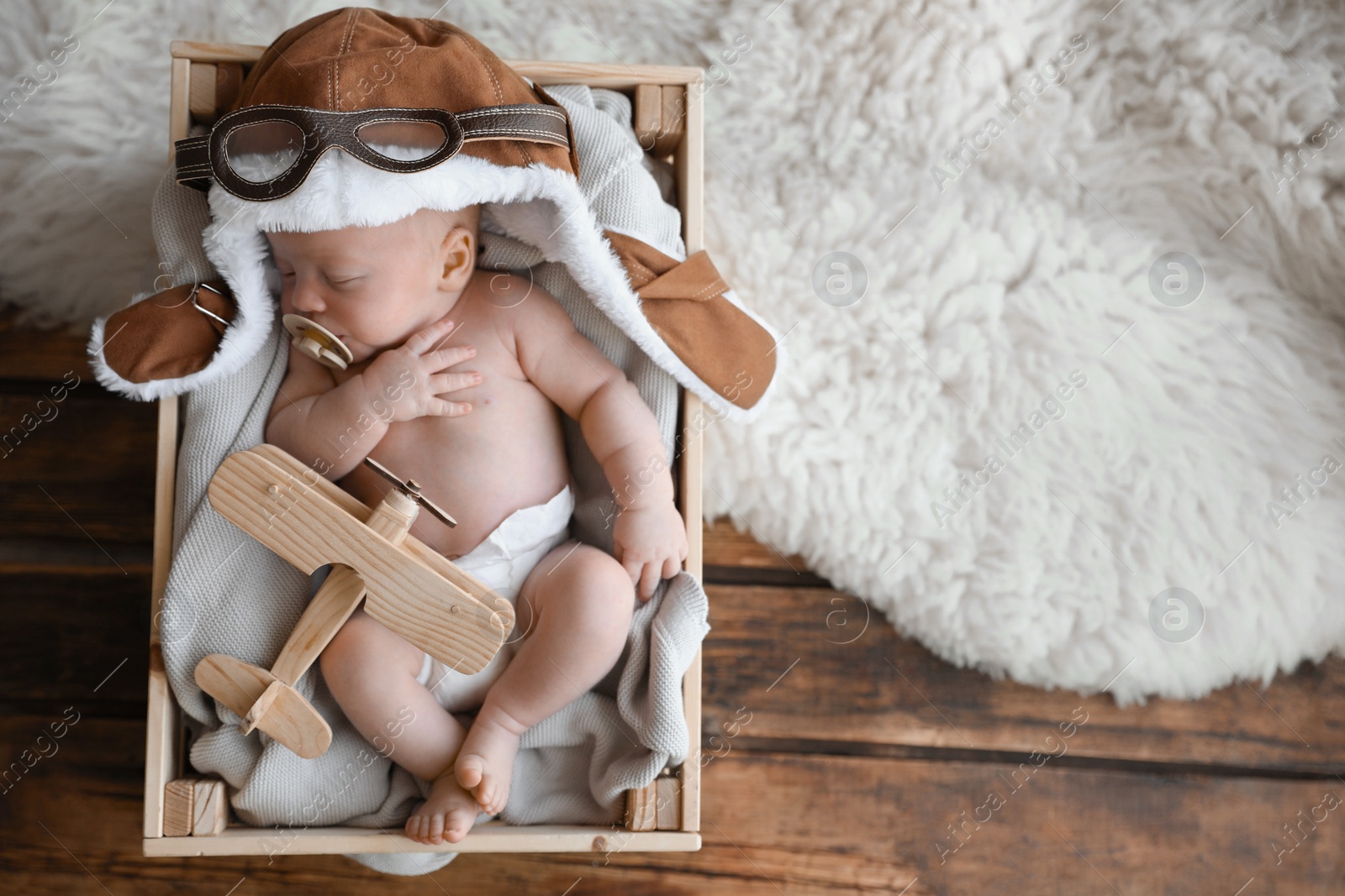 Photo of Cute newborn baby wearing aviator hat with toy sleeping in wooden crate, top view. Space for text