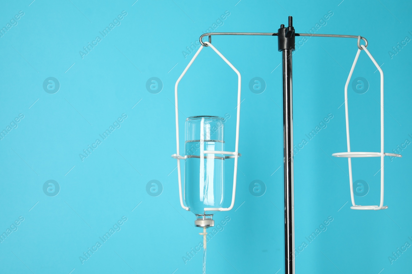 Photo of IV infusion set on pole against light blue background. Space for text