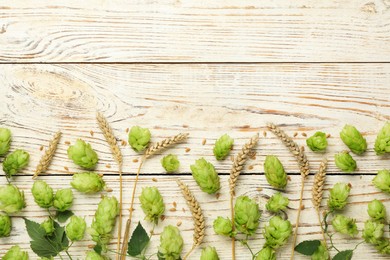 Flat lay composition with fresh green hops and wheat ears on white wooden table, space for text