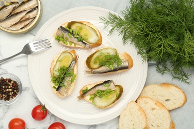 Photo of Delicious sandwiches with sprats, pickled cucumber, green onion and dill served on white marble table, flat lay