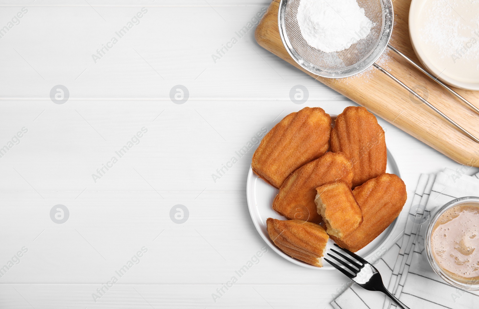 Photo of Delicious madeleine cakes, powdered sugar and drink on white wooden table, flat lay. Space for text