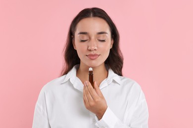 Beautiful young woman with bottle of essential oil on pink background