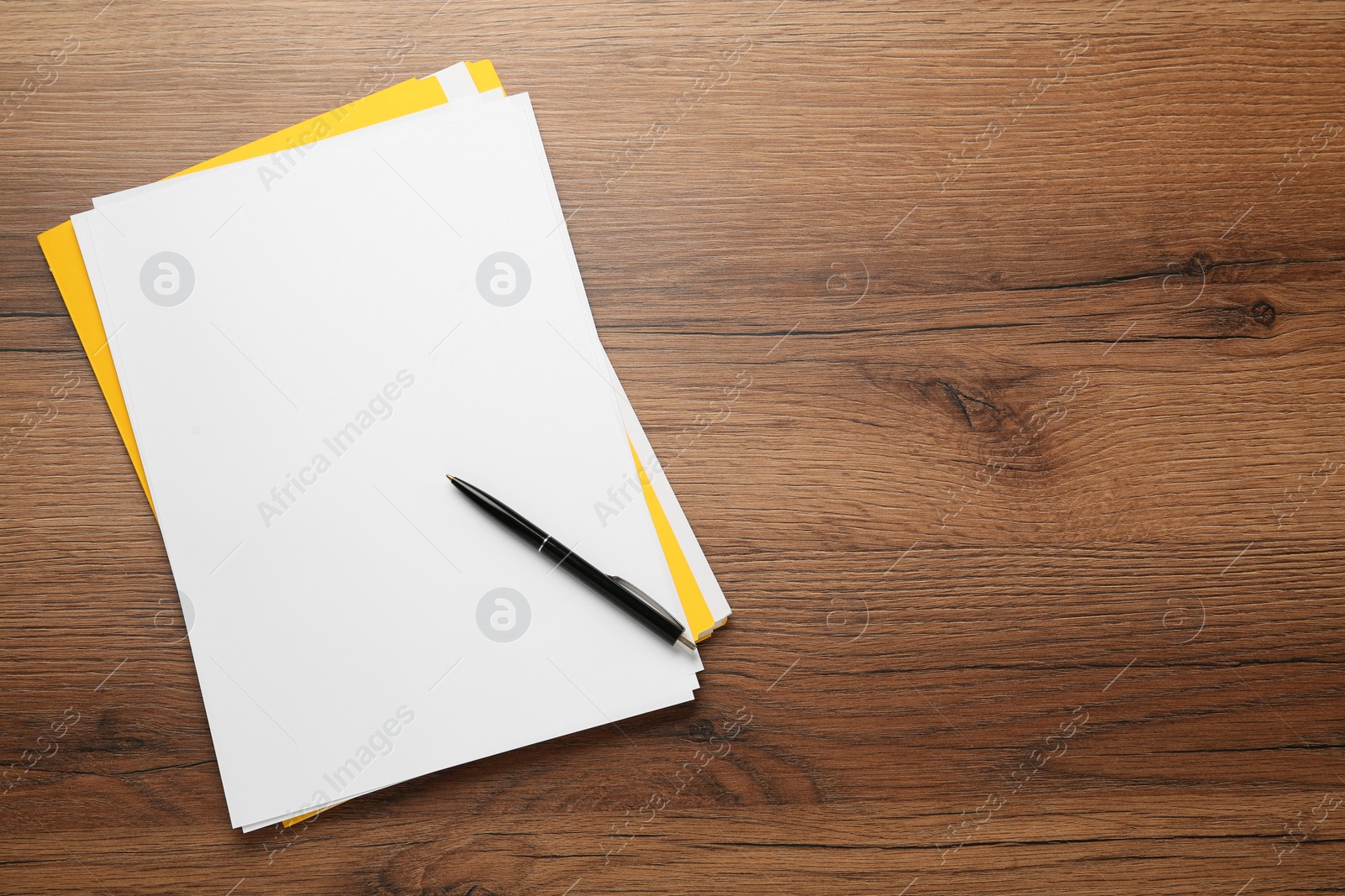 Photo of Yellow file, blank sheets of paper and pen on wooden table, top view. Space for text