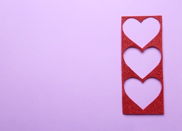 Photo of Red shiny hearts stencil on violet background, top view. Space for text