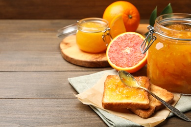 Photo of Delicious toasts, orange marmalade and fresh fruits on wooden table. Space for text