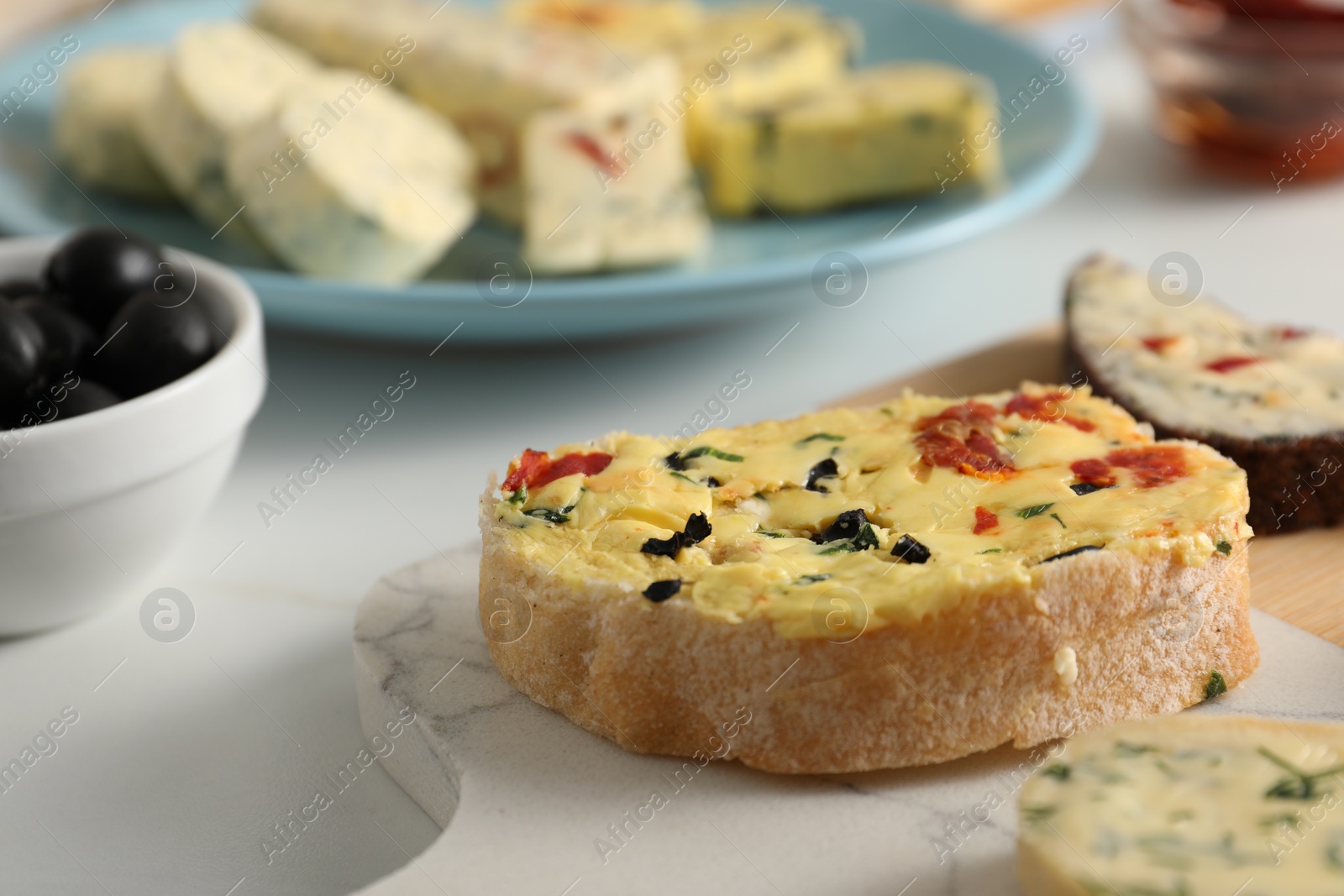 Photo of Tasty butter with olives, chili pepper and bread on white table, closeup