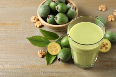 Photo of Fresh feijoa smoothie in glass on wooden table, closeup. Space for text