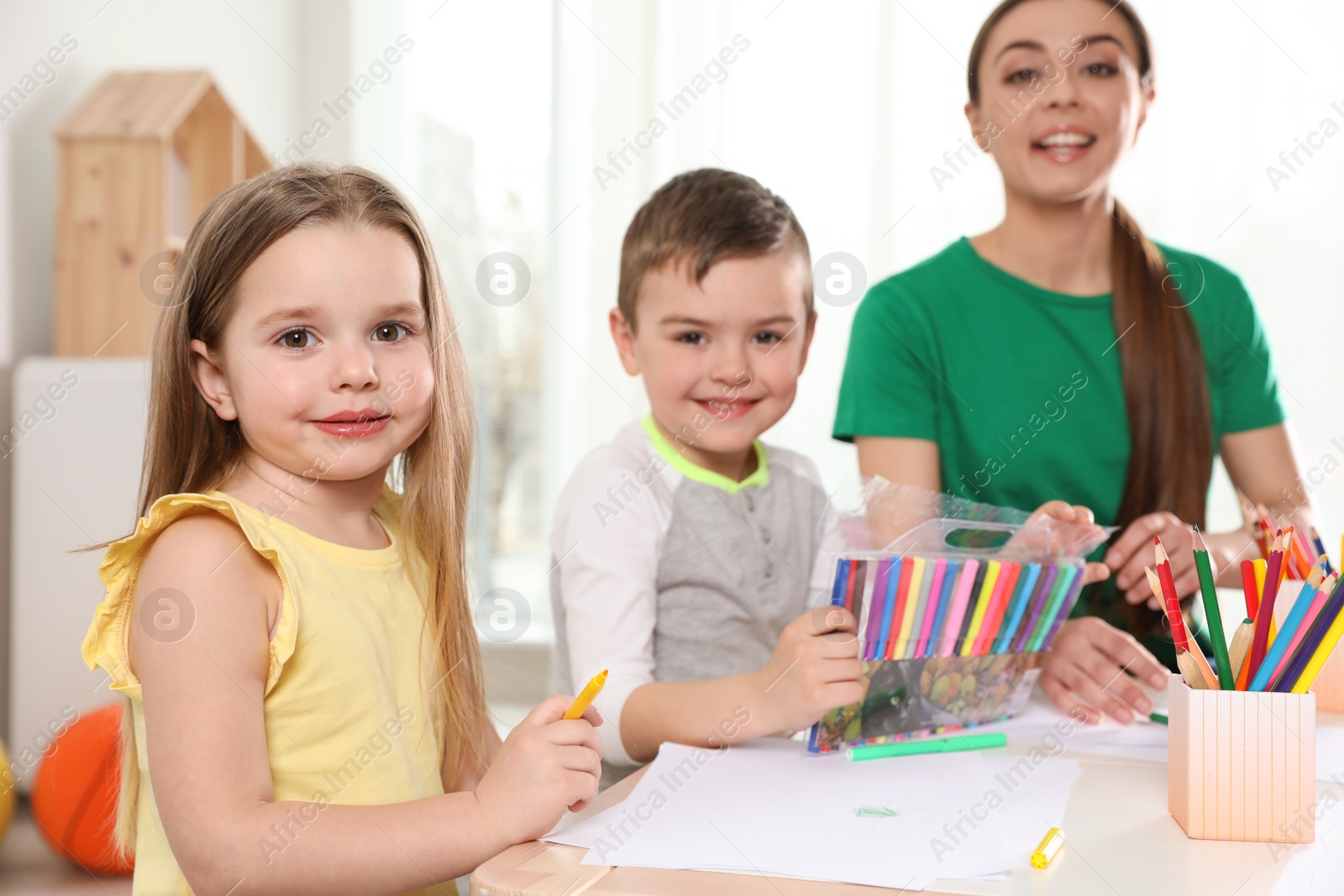 Photo of Little children with kindergarten teacher drawing at table indoors. Learning and playing