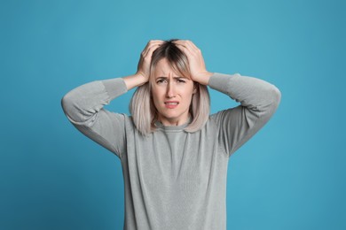 Woman suffering from headache on light blue background