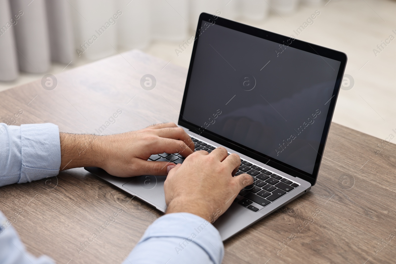 Photo of E-learning. Young man using laptop at wooden table indoors, closeup