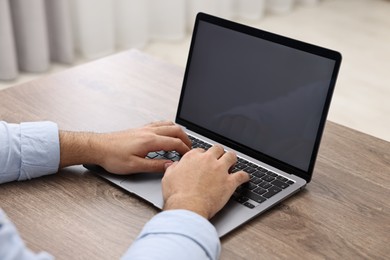 Photo of E-learning. Young man using laptop at wooden table indoors, closeup