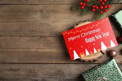 Flat lay composition with greeting card and Christmas decor on wooden background, space for text