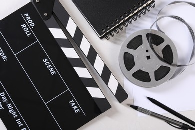 Movie clapper, film reel, notebook and pens on light table, flat lay