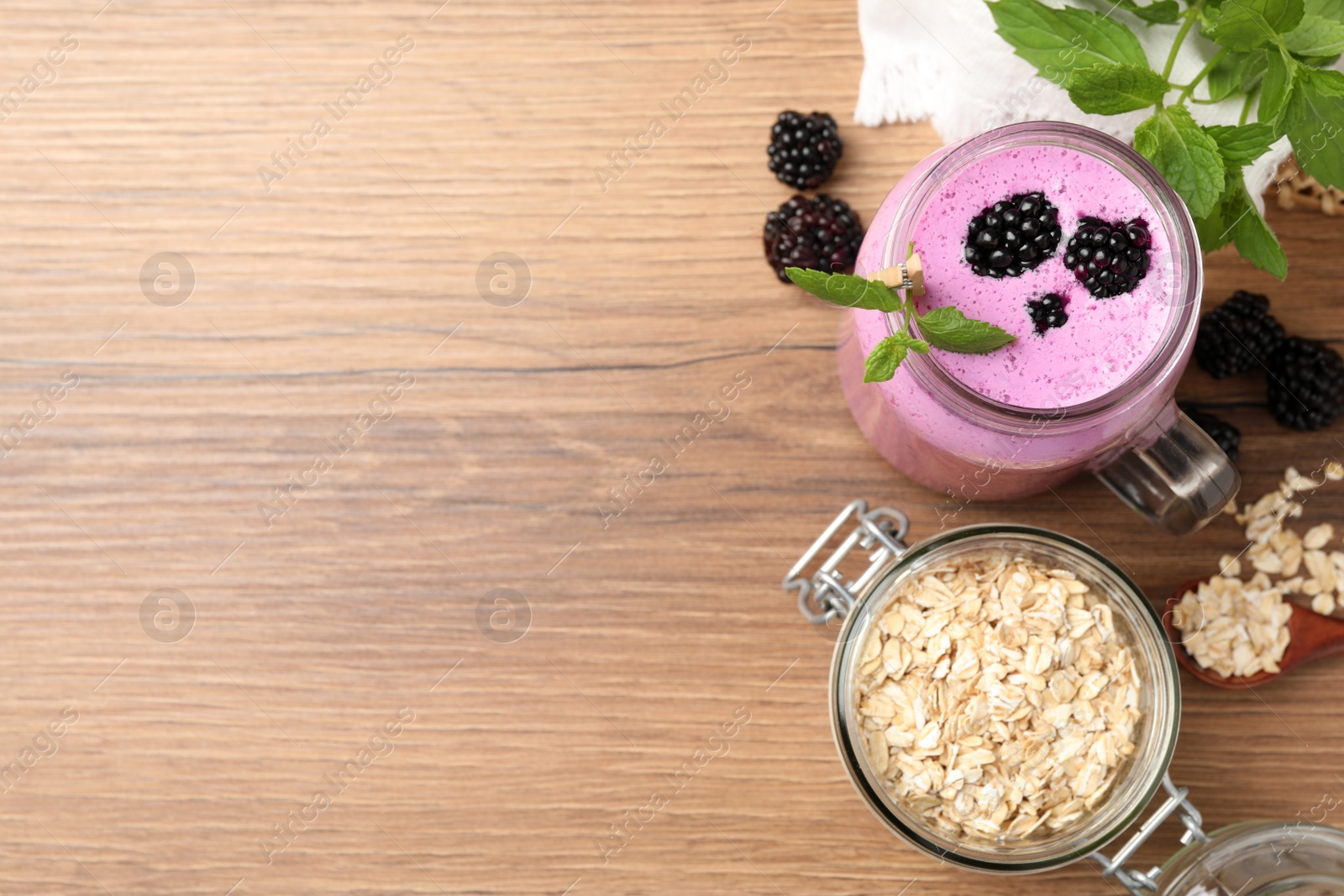 Photo of Delicious blackberry smoothie, oatmeal and berries on wooden table, flat lay. Space for text
