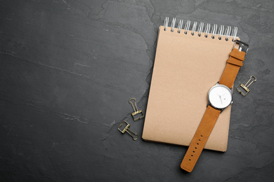 Photo of Kraft notebook and stylish wristwatch on black table, flat lay. Space for text