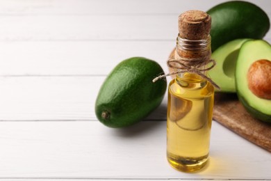 Photo of Glass bottle of cooking oil and fresh avocados on white wooden table, closeup. Space for text