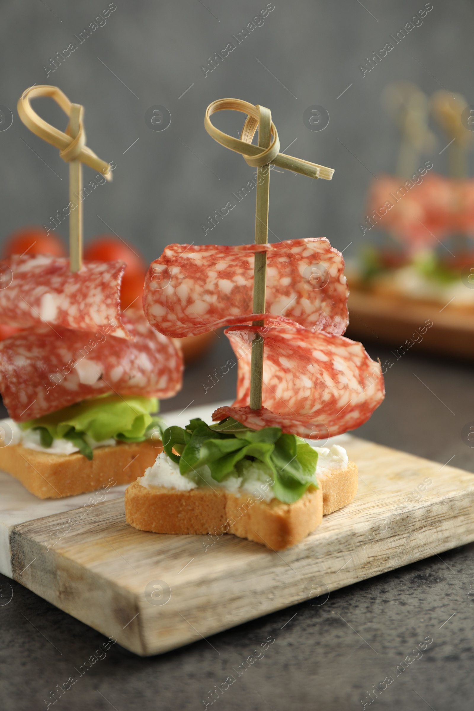 Photo of Tasty canapes with salami, greens and cream cheese on grey table, closeup