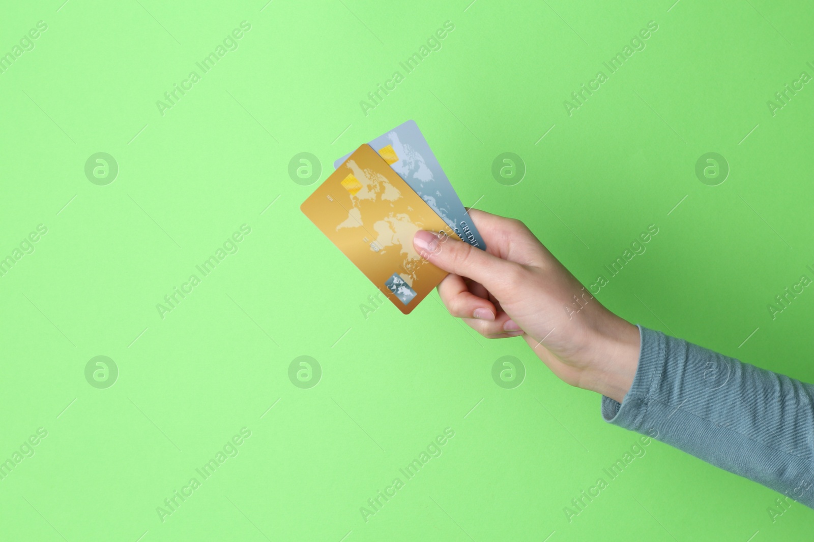 Photo of Woman holding credit cards on light green background, closeup