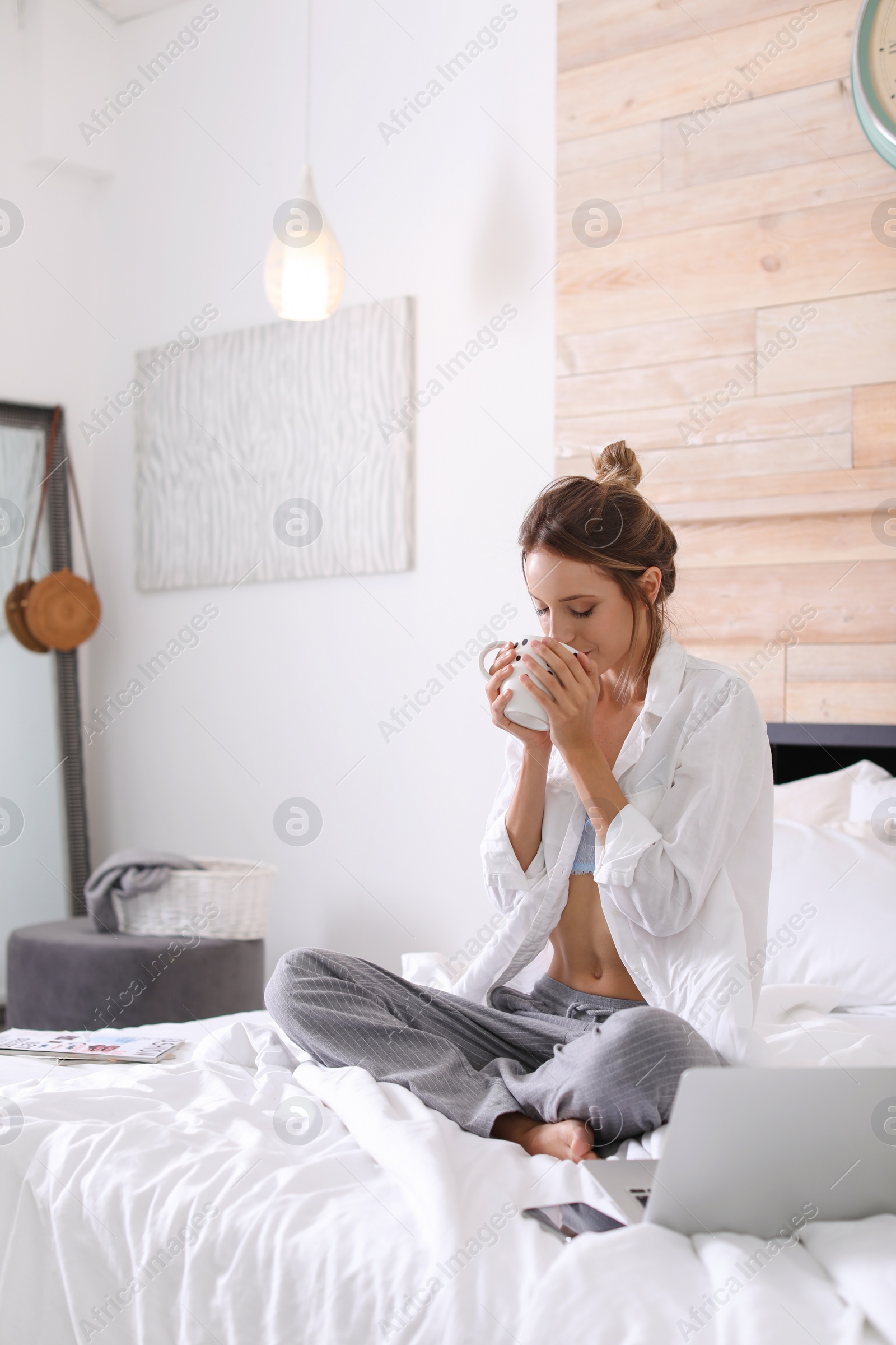 Photo of Young happy woman with cup of aromatic coffee on bed at home. Lazy morning