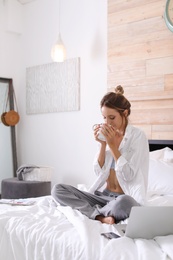 Young happy woman with cup of aromatic coffee on bed at home. Lazy morning