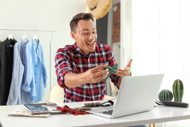 Photo of Male fashion blogger with bow tie and laptop at home. Online broadcast