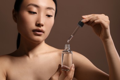 Photo of Beautiful young woman with bottle of cosmetic serum on brown background, closeup