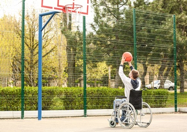 Young man in wheelchair playing basketball on sports ground