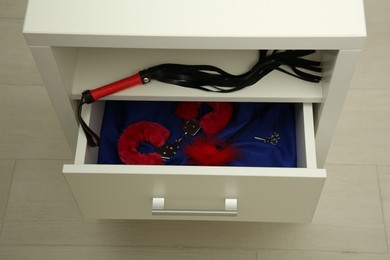 Whip, furry handcuffs and feather tickler in drawer indoors. Sex toys