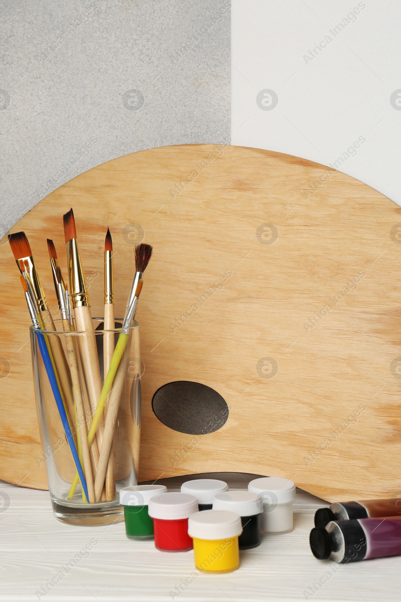 Photo of Artist's palette, colorful paints and brushes on white wooden table