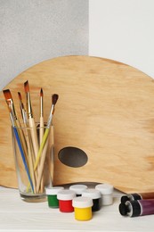 Photo of Artist's palette, colorful paints and brushes on white wooden table