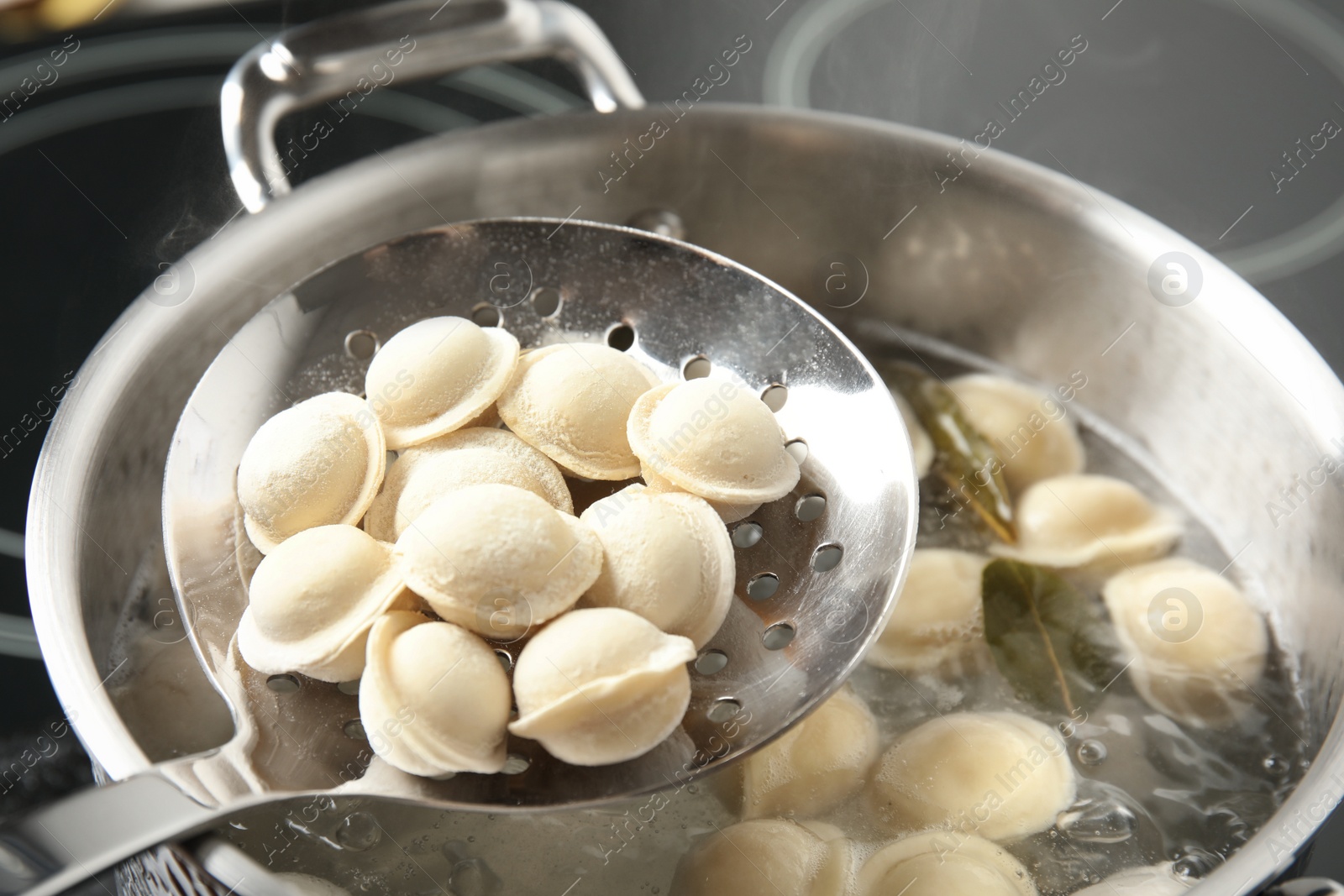 Photo of Closeup of dumplings on skimmer over stewpan with boiling water. Home cooking