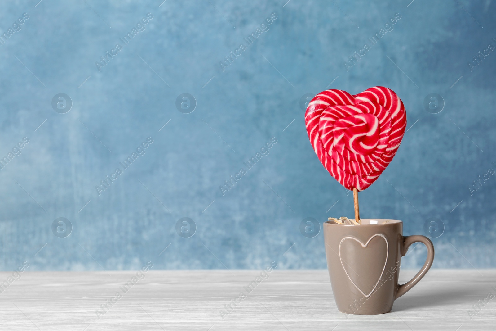 Photo of Sweet heart shaped lollipop in cup on table. Space for text