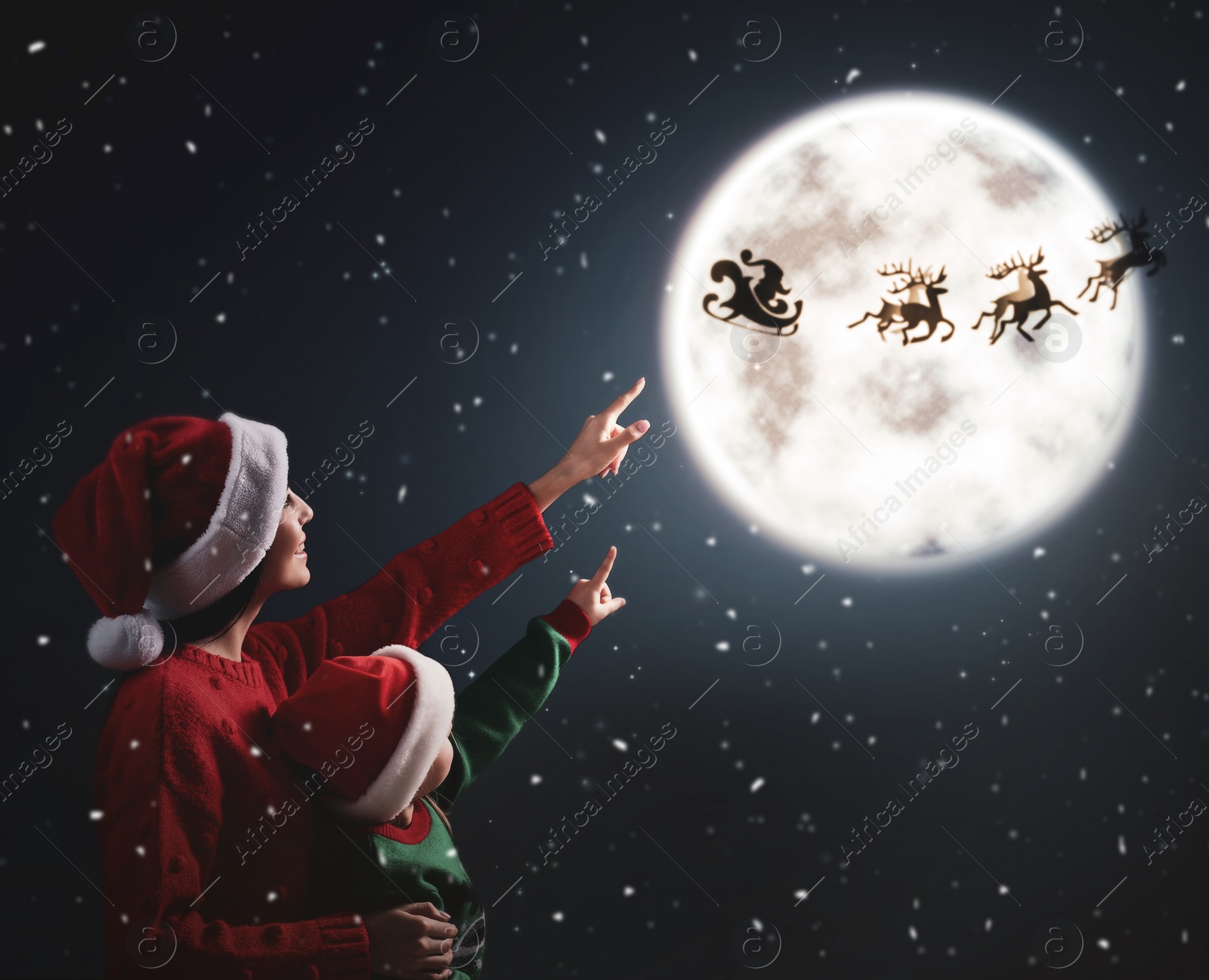 Image of Mother and her little daughter looking at Santa Claus with reindeers in sky on full moon night. Christmas holiday