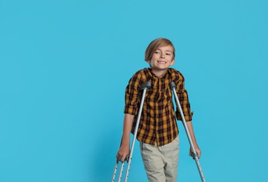 Photo of Portrait of happy boy with crutches on light blue background. Space for text