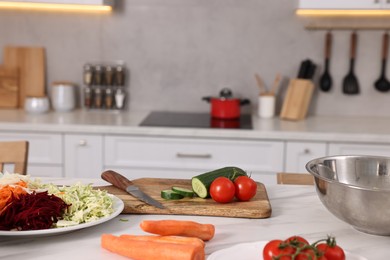 Photo of Cooking vegetarian meal. Fresh vegetables, knife, board and bowl on white marble table in kitchen