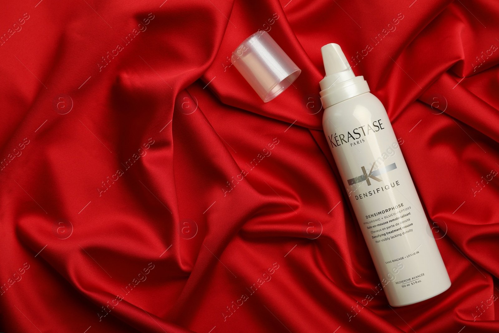 Photo of MYKOLAIV, UKRAINE - SEPTEMBER 08, 2021: Bottle of Kerastase hair care cosmetic product on red fabric, flat lay. Space for text