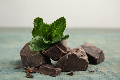 Photo of Tasty dark chocolate pieces with mint on blue wooden table