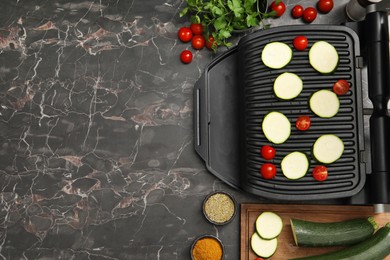 Electric grill with vegetables and spices on black marble table, flat lay. Space for text