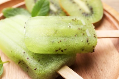 Photo of Tasty kiwi ice pops on wooden plate, closeup. Fruit popsicle