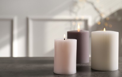 Photo of Different burning candles on grey table indoors. Space for text