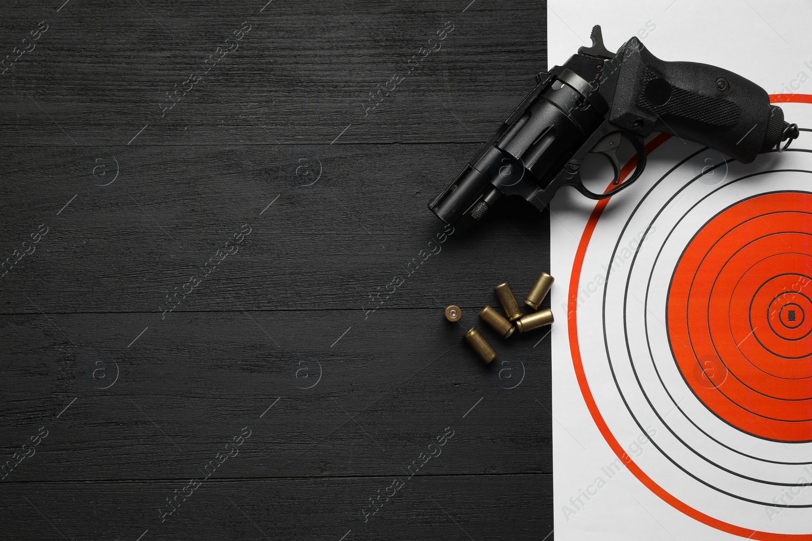 Photo of Shooting target, handgun and bullets on black wooden table, top view. Space for text