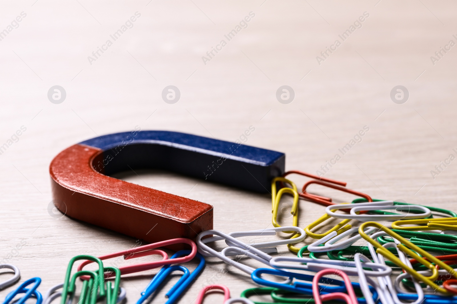 Photo of Magnet attracting colorful paper clips on light wooden background, closeup